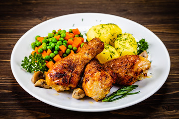 Grilled chicken drumsticks with vegetables on wooden background