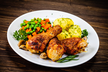 Fototapeta premium Grilled chicken drumsticks with vegetables on wooden background