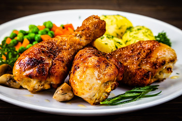 Grilled chicken drumsticks with vegetables on wooden background