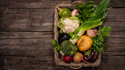 Basket with vegetables on a wooden background. Cauliflower, broccoli, radish, parsnip, leek, kohlrabi