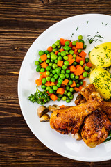 Grilled chicken drumsticks with vegetables on wooden background