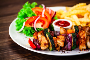 Kebabs - grilled meat with french fries and vegetables wooden background