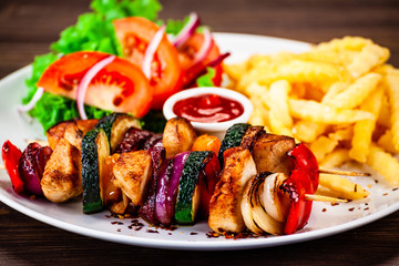 Kebabs - grilled meat with french fries and vegetables wooden background