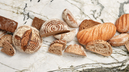 Whole and pieces of different homemade organic bread on a gray marble background with copy space. Flat lay