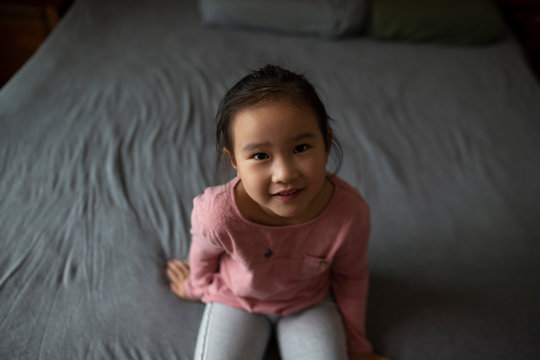 Little Asian Girl Sitting Indoor Looking Up To The Camera