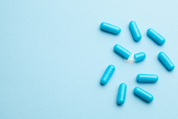 Blue tablets in capsules. One capsule is open. Blue background. Copy space for text.