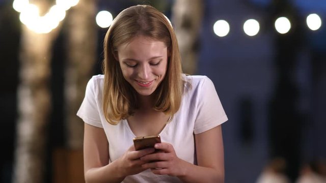 Young attractive interested girl is typing message on her smartphone in evening in summer, smiling, communication concept.