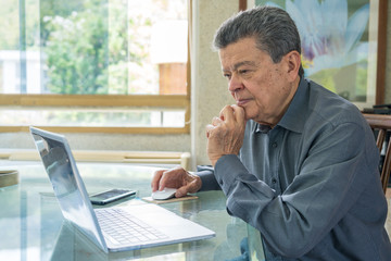 Hispanic senior man working at home office with laptop computer. Home office concepts
