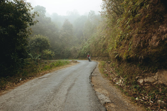 Motorcyclist on the asphalt road riding through foggy forest
