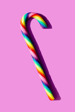Simple still-life of a rainbow-colored candy cane on a light magenta background