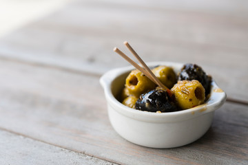 black and green olives in white bowl with wooden stick. On white table, space for text