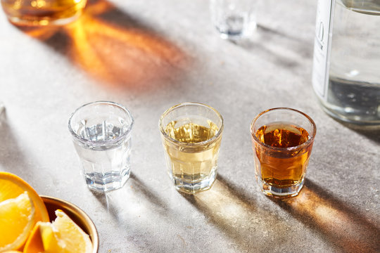 Different types of tequila in a row on grey surface.
