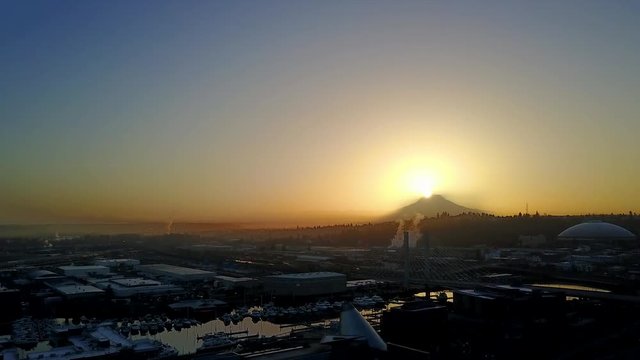 Swooping aerial shot over Tacoma, Washington with the sunrise peaking over Mount Rainier.