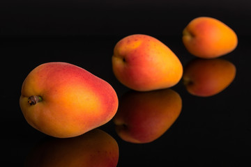 Group of three whole fresh orange apricot placed diagonally in line isolated on black glass