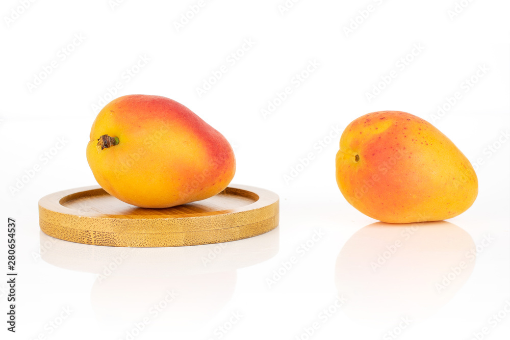 Wall mural group of two whole fresh orange apricot on a round bamboo coaster isolated on white background