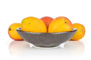 Group of five whole fresh orange apricot , two of them are aside and the other three are in a dark ceramic bowl isolated on white background