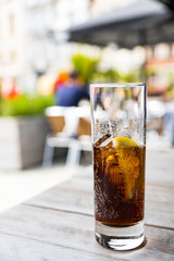 long drink glass with cola, slice of lemon and ice cubes