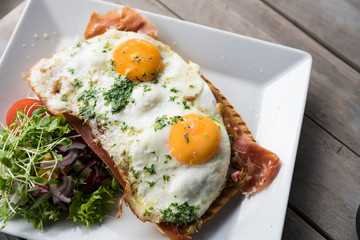 Meat sandwich with fried eggs, salad on white plate and wooden table