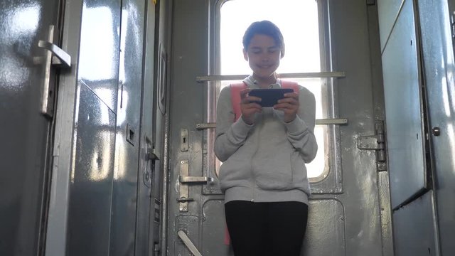 teenager girl traveler with backpack stands by the window of the train car with a smartphone. travel transportation railroad concept. the girl in the train at the window corresponds the girl in the