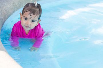 Fototapeta na wymiar Baby girl of two years old tires swimming in a swimming pool. She is happy and playful with her experience.