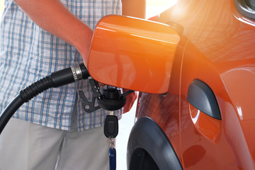 Pumping gasoline fuel in orange car at a gas station. To fill car with fuel in petrol station. Petrol station pump. Sunny.