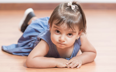 Naklejka premium Baby girls of two poses for studio portraits. She is wearing a jean dress. She is lying on the floor and playing.