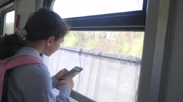 girl teenager traveler with backpack stands by the window of the train car with a smartphone. travel transportation lifestyle railroad concept. the girl in the train at the window corresponds the girl