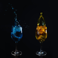 Glasses with blue and yellow water on a black background. Splashing water. Additional colors.