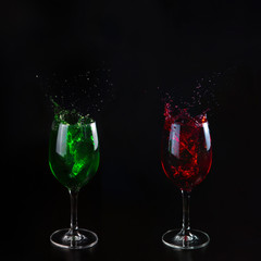 Glasses with red and green water on a black background. Splashing water. Additional colors.