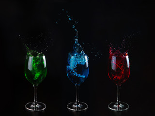 Three primary colors: red, green, blue. Glasses with multicolored water on a black isolated background. Splashing water.