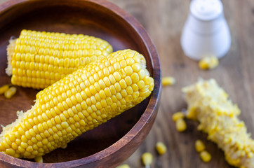 Cooked corncobs are on a dark wooden plate,