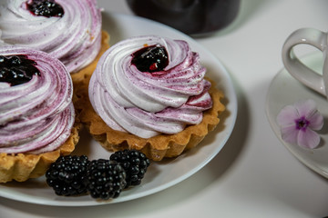 Sweet tartlet with meringue and blackberry jam and phlox flowers on white background closeup