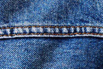 Blue denim jeans with middle brown yellow color sewing thread seam macro closeup textile background.