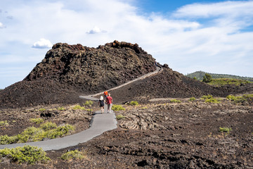 Hikers walk up the Spatter Cones trail, a paved walkway leading to a cinder cone wi in Craters of the Moon National Monument in Idaho © MelissaMN