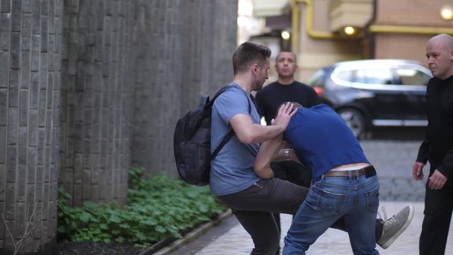 Close-up of armed criminals attacking male walking in city street. Fearless man knocking three muggers applying Krav Maga self defence and running away