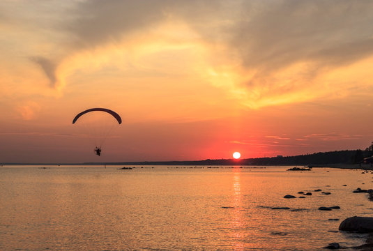Sunset over the sea. Reflection of the sun in water. Silhouette of paraglider flying in the sky. Sunset beach in a summer evening. Gulf of Finland, Baltic sea, Komarovo, Saint-Petersburg, Russia.