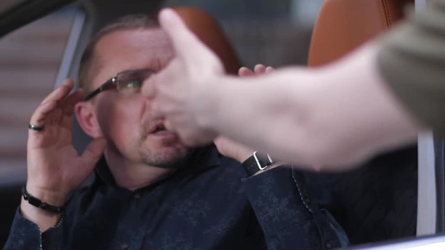Close-up of man driving car being attacked by mugger with firearm. Angry fearless driver repelling attack grabbing gun and punching criminal for attempt of armed hijacking