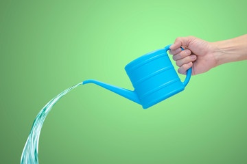 Man's hand holding blue watering can with falling water, isolated on green background.
