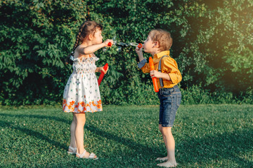 Funny Caucasian children girl and boy blowing soap bubbles in park at summer sunset. Real authentic...