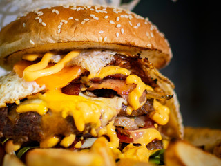 foreground double beef burger with cheddar cheese and bacon and sesame seed bun