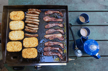 Fresh pot of coffee with bacon, sausage and hashbrowns cooking on a hot grill
