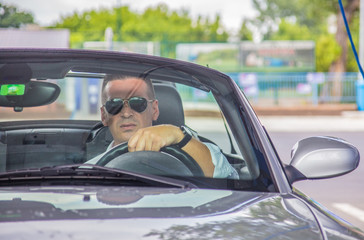 A handsome man driving cabriolet and wearing glasses 