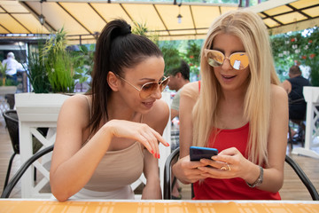 two female friends drinking coffee in cafe and holding phones 