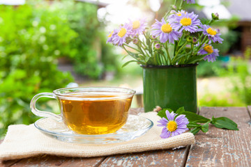Tea herbal useful for health on on canvas, on a wooden table, next to the lilac flowers in a metal mug. Against the nature of the countryside in the sun.
