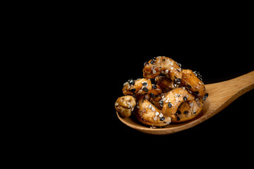 Sesame Coated Cashew Nuts on wooden spoon. Isolated on black background
