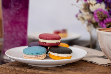 Choose the focus on the latte, art, and macarons on the wooden tray and on the table with a black stripe on the dust.