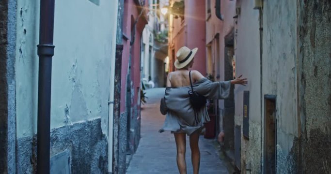 Charming romantic lady walking through amazing italian town enjoying cityscape in the evening. Back view of delighted young woman wandering in the narrow street. Rio Majore, Liguria, Italy