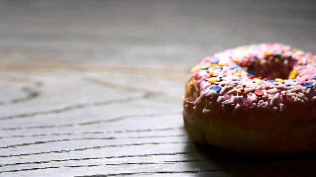 Delicious donut falls on a wooden surface. Slow motion