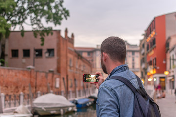 Travel blogger with a bag making phone photo of venice canal for social media 