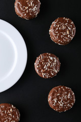 Chocolate cookies with coconut shaving chocolate coating and coconut on wooden black  background.